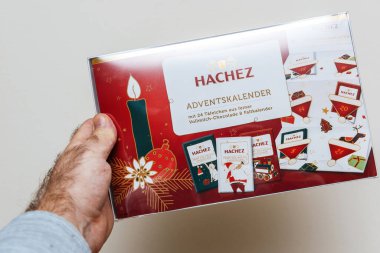 Bremen, Almanya 10 Aralık 2023: Bir erkek eli, içinde leziz çikolatalarla dolu Hachez takvimini incelikle tutuyor ve bayram sezonunda günlük hoşgörü sözü veriyor.