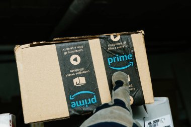 Bremen, Almanya - 10 Aralık 2023: Eldiven giyen bir depo işçisi, çalışma ve paket teslimi kavramını gösteren Amazon Prime karton paketinin üzerindeki Prime logosunu işaret ediyor