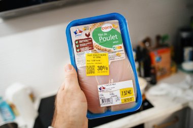 Paris, France - Jan 12, 2024: In a modern kitchen, a male hand holds an Auchan Filet de Poulet with Nutri-Score A, featuring a special 30 percent discount due to its soon approaching expiration date. clipart