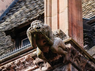 Tarihi bir binanın kenarına tünemiş gizemli bir heykel, taştan yüzeyi ile şehre bakıyor..