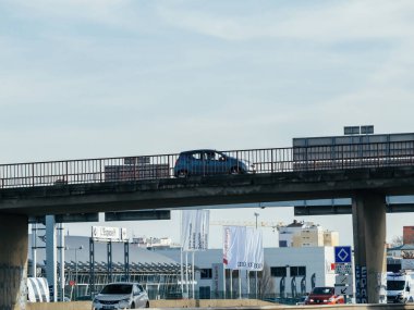 Strasbourg, Fransa - 20 Mar 2024: Strasbourg 'da Fransız köprüsünden geçen küçük bir araba, arka planda birden fazla otomotiv galerisi bulunan, kentsel otomotiv sahnesini gözler önüne seren