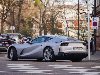 Strasbourg, Fransa - 20 Mart 2024: Parlak, gümüş renkli, Ferrari marka bir araba yol kenarında gidiyor, güneş ışığını yansıtıyor, etrafta kimse yok..