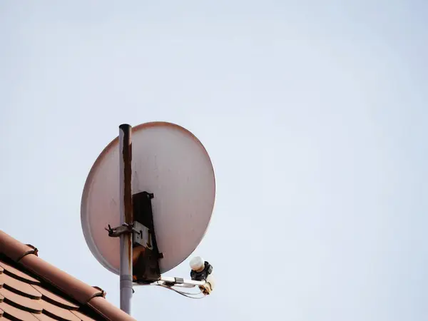 A satellite dish mounted on a pole on top of a rooftop, ready to receive signals for television or internet services.
