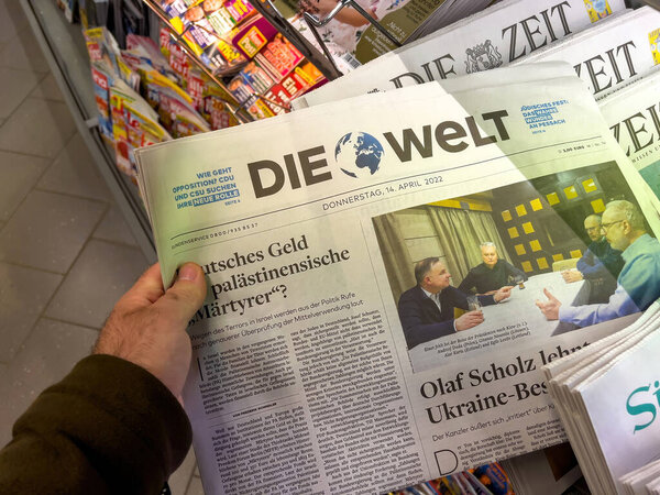 Frankfurt, Germany - Apr 14, 2022: Hand holding an edition of DIE WELT newspaper, with a headline about German funds and Palestinian martyrs, touching on contentious issues