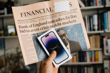 Londra, Birleşik Krallık - 29 Eylül 2022: En son Apple iPhone 14 Pro 'yu elinde tutan bir erkek aynı zamanda İngiltere Merkez Bankası' nın 57 milyar teklifiyle ilgili manşetlerde yer alan Financial Times 'ı da yayınlıyor