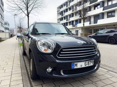 Freiburg im Breisgau, Almanya - 7 Mart 2024: Siyah bir Mini Cooper konut binalarıyla dolu bir caddeye park etmiş, bahar manzarası sergiliyor.