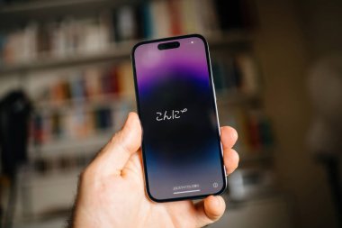 Londra, Birleşik Krallık - 29 Eylül 2022: Ekranda Japonca metni gösteren iPhone Pro 'yu tutan bir elin yakın çekimi. Arka plan bulanık, kapalı bir odada rafları gösteriyor.