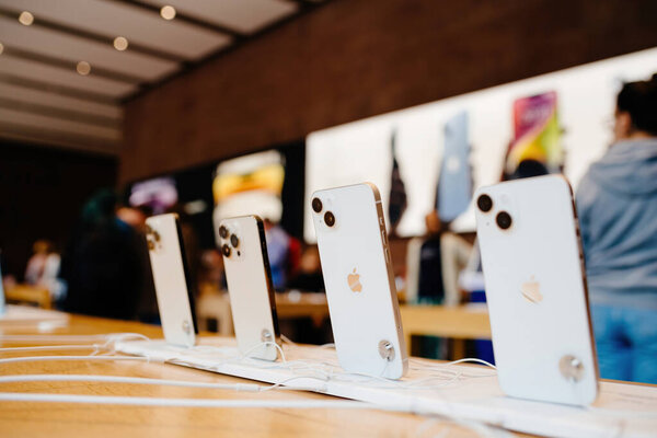 Париж, Франция - 28 октября 2024: Ряд последних компьютеров Apple и iPhone отображается в Apple Store, с силуэтами людей на заднем плане, подчеркивая гладкий дизайн и передовые