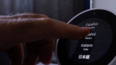 Paris, France - Jun 5th, 2020: A male hand presses the Amazon Alexa display to select a language, with options including Spanish, Italian, Chinese, and dialects from Spain and Mexico, highlighting the clipart