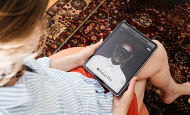 Londra, Birleşik Krallık - 11 Haziran 2023: Bir kadın oturma odasında rahatça oturup iPad Pro 'sunda Apple Vision Pro karışık gerçeklik kulaklığını okuyarak ekranda gösterilen özellikleri keşfediyor.