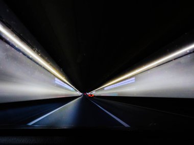 Bulanık ışıklar ve yüksek hız hissiyle gece tünelin içinden dinamik bir manzara. Tünellerin ışıklandırılması, yol mesafeye daraldıkça geleceksel ve dramatik bir etki yaratıyor.