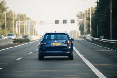 Hollanda - 27 Ağustos 2019: Mavi bir Skoda Superb arka planda birden fazla araçla Hollanda otoyolunda seyahat ediyor. Sahnede hava açık, yol kenarındaki yeşillik ve yol kenarındaki elektrik direkleri yer alıyor.