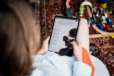 Paris, Fransa - 11 Haziran 2023: Bir kadın oturmuş iPad 'de Apple Vision Pro' yu okuyor ve yerdeki çocuk oyuncaklarıyla çevrili kulaklığın detaylı özelliklerine odaklanıyor.