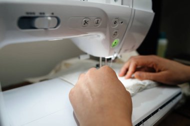 Eller dikiş makinesinde kumaşa rehberlik etmek için titizlikle çalışırlar. Dikiş işleme sürecinde gerekli olan detaylara dikkati gösterir.