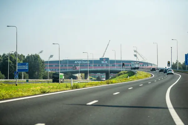 stock image Netherlands - Aug 27, 2019: A view of the AFAS Stadion from a Dutch highway with vehicles approaching. Road signs indicate directions to Ring Alkmaar West and Boekelermeer, with a clear sky overhead