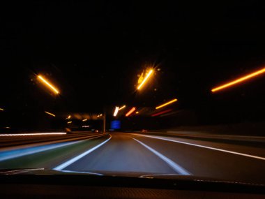 Sokak lambalarından gelen ışık çizgileriyle ve geçen araçlarla Hollanda 'da hız ve gece sürüşünün özünü yakalayarak dinamik bir hareket yaratan bir gece otoyolu sahnesi.