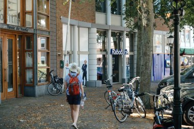 Texel, Hollanda - 27 Ağustos 2019: Hollanda 'nın Texel belediyesindeki Tusse de Banke sergisi yakınlarında yürüyen meraklı kadın, arka planda Rabobank ve birçok bisikletle