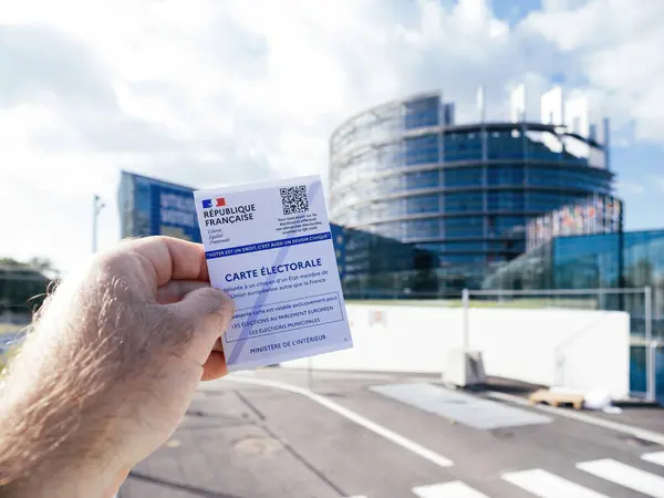 stock image Strasbourg, France - Jun 6, 2024: A person holding a French electoral card with a QR code in front of the European Parliament building in Strasbourg, emphasizing the civic duty and importance of