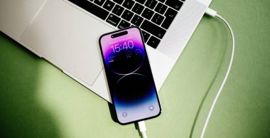 Paris, Fransa - Sep 29, 2022: Bir iPhone 15 Pro USB-C kablosu kullanarak bir MacBook Pro 'ya bağlandı, bir gradyan mor ve mavi ekran gösteriyor, Lightning port' tan USB-C 'ye geçişi gösteriyor