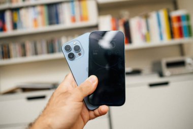 Paris, Fransa - 29 Eylül 2022: İki nesil boyunca iPhone Pro akıllı telefonları elinde tutan adam büyük bir kütüphane geçmişine karşı, teknolojinin evrimini vurguluyor