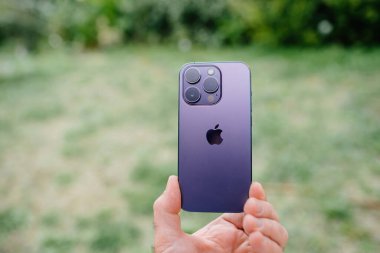 Paris, Fransa - 29 Eylül 2022: Mor titanyum Apple iPhone 15 Pro akıllı telefon yeşil bahçe arka planına karşı, gösterişli teknoloji ve doğa arasındaki zıtlığı vurguluyor