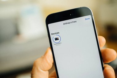 Paris, Fransa - 29 Eylül 2022: Akıllı telefonu tutan bir el, AirDrop ekranını ve mevcut cihazların listesini gösteriyor. Telefon MacBook Pro 'ya bir kopyasını göndermek üzere..