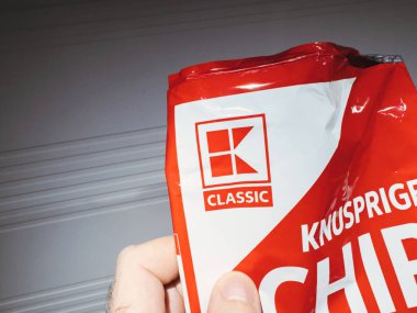 Münih, Almanya - 13 Mart 2024: Kaufland çipleri paketini elinde tutan bir erkeğin POV görüntüsü, özellikle plastik kutunun üzerinde Kaufland zinciri logosu yer alıyor, markaların kimliklerini ve