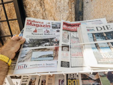 Valldemossa, İspanya - 8 Temmuz 2024: Sarı saati olan bir erkek, Mallorca, İspanya 'daki bir basın standında Neustart Mallorca ve yerel olaylarla ilgili manşetler içeren bir sayı yayınladı..