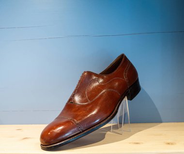 Dekoratif dikişleri ve delinmiş başparmak detaylarıyla eski kahverengi deri ayakkabılar ahşap bir zeminde mavi arka plana karşı sergileniyor, zarif tasarımı ve...