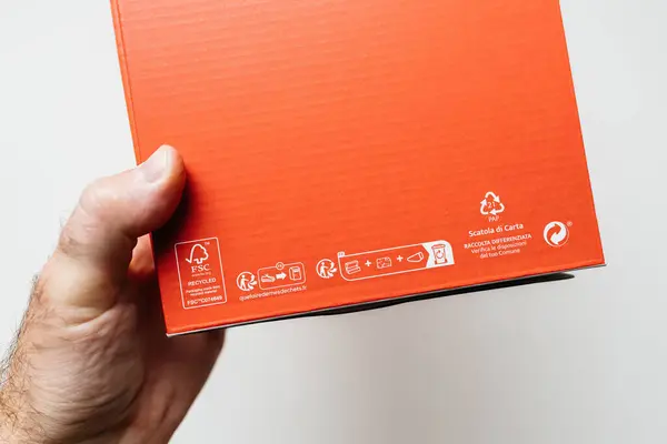 stock image Paris, France - May 29, 2024: A hand holds an orange cardboard box, focusing on its recycling and FSC certification symbols. The boxs surface includes instructions for proper disposal and