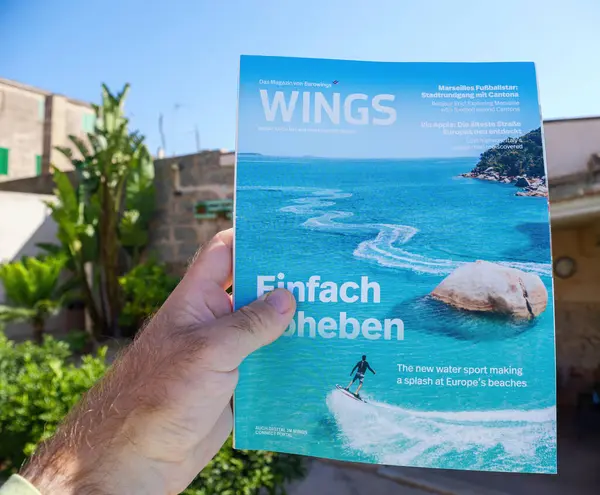 stock image Palma, Spain - Jul 10, 2024: A male hand holds the Wings magazine by Eurowings, owned by Lufthansa, in a Mallorca finca, blending travel luxury with a serene, rustic setting