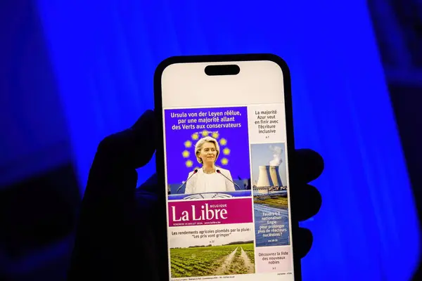 stock image Paris, France - Jul 20, 2024: A person holding a smartphone displaying the La Libre newspaper cover featuring Ursula von der Leyens reelection, set against a blue background, with additional