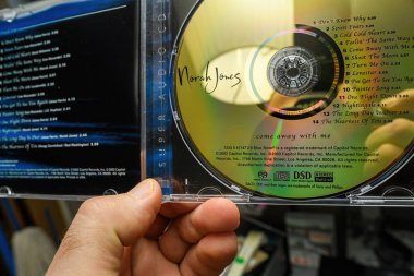 Paris, France - Mar 18, 2024: Close-up of a male hand holding an SACD Super Audio DSD disk of Norah Joness Come Away With Me highlighting the high-quality audio format and the album cover clipart