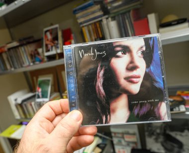Paris, Fransa - 18 Mart 2024: Arka planda Vitsoe raflarında çoklu SACD diskleri olan Norah Joness Come Away with Me 'nin SACD Super Audio DSD diskini tutan bir erkeğin POV' u