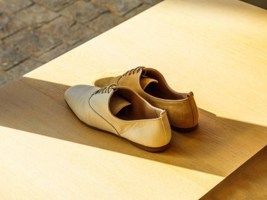 Ahşap raflarda sergilenen bir çift lüks kadın ayakkabısı, üzerine zıt gölgeler düşüyor, üst düzey bir perakende piyasasında zarif ve sofistike bir sunum yaratıyor.