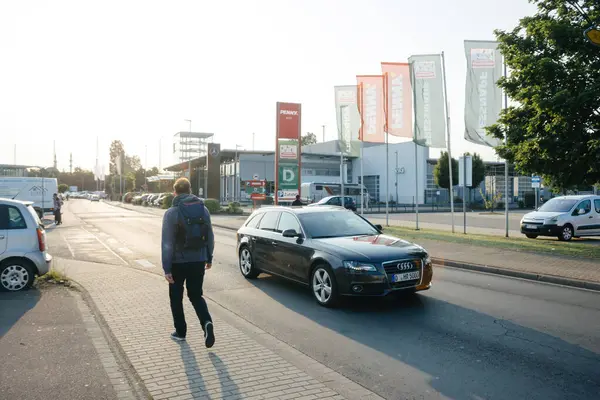 stock image Kehl, Germany - May 27, 2023: Rear view of a male with a backpack walking near a Penny store, a Mercedes-Benz dealership, and other shops in the parking area of the German city of Kehl, capturing the