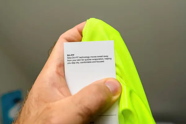 stock image Paris, France- Jun 30, 2024: A male hand holding a vivid green Nike Dri-Fit technology T-shirt, with a sticker explaining the advantages of the sweat-wicking technology, emphasizing the products