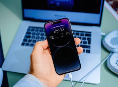 Paris, Fransa - 28 Ekim 2022: Arka planda MacBook Pro ile birlikte USB-C bağlantısı bulunan yeni Apple iPhone 15 Pro 'yu tutan bir erkeğin POV' u. iPhone 15 ilk Pro modelidir.