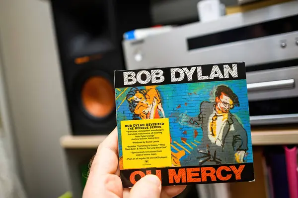 stock image Paris, France - Mar 18, 2024: Male hand holding Bob Dylans Oh Mercy SACD from the Revisited series with a hi-fi audiophile setup visible in the background