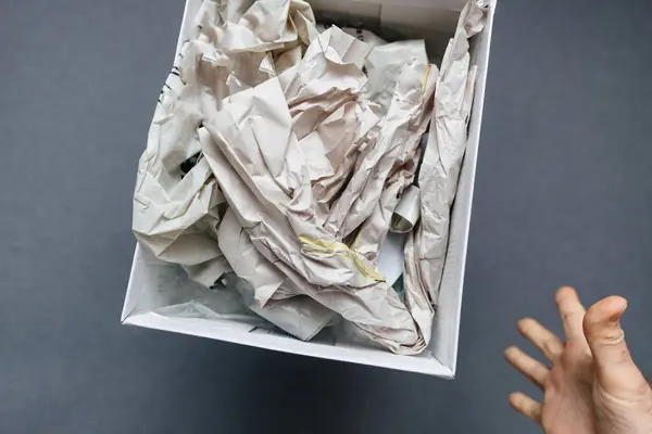 stock image A male hand reaching to catch a paper file box floating against a gray background, capturing the motion and effort to grasp the object in mid-air