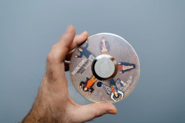 Paris, France - Apr 6, 2024: POV of a male hand holding rolling stones through the through the past darkly Sacd DSD disk against a blue background, showcasing a blend of music and technology clipart