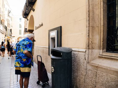 Palma, Mallorca 8 Temmuz 2024: Yaşlı bir adam Palma de Mallorca 'daki Banca March binasının yakınındaki bir çöp kutusunun yanında duruyor, günlük rutini tarihi kentsel düzenle harmanlıyor