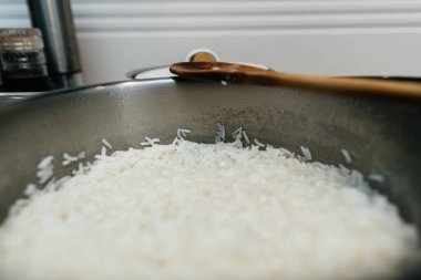 Metal bir tencerede kaynamış beyaz pirinç manzarası, kenarında bir tahta kaşık, buhar ve yoğunlaşma var..