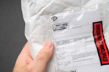 Paris, Fransa - 24 Aralık 2024: Kapalı kırmızı etiketli bir paket zarfını tutan bir erkeğin yakın çekimi, paketin varış anını ve güvenli bir şekilde ele alınış anını vurguluyor