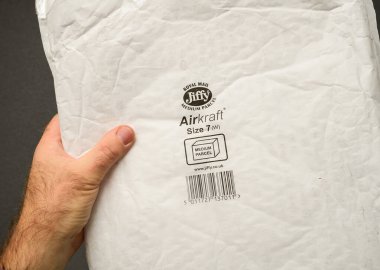 Paris, Fransa - 12 Aralık 2024: Bir erkek, gri bir arka planda, güvenli ambalajı gösteren, hava saldırısı korumalı Royal Mail Jiffy orta paketini elinde tutuyor