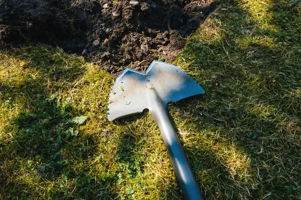 Bahçenin yenilenmesi sırasında çimlerin yanında duran küreğin havadan görünüşü, çevreleyen toprak ve aletler devam eden peyzaj çalışmalarını gösteriyor.