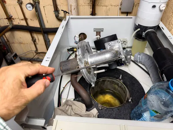 stock image A man inspecting and repairing a gas boiler, preparing it for the upcoming winter season by cleaning the open gas chamber, ensuring efficient and safe operation