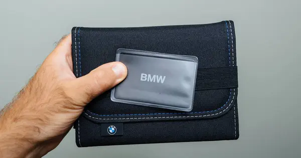 stock image Munich, Germany - Sep 2, 2024: A male car owners hand holds the BMW Car Connectivity Consortium CCC Digital Key above the stylishly designed packaging of the cars instruction manual, highlighting