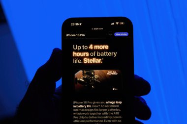 Paris, Fransa - 8 Ekim 2024: iPhone 16 Pro Max 'i elinde tutan bir erkeğin dikey çekimi mavi arka planda, Stellar sloganı ve 4 saat daha fazla pil ömrü vurgulanıyor