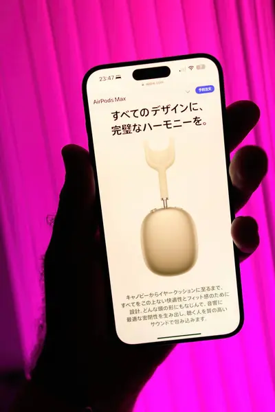 stock image Paris, France - Sep 8, 2024: Male hand holding the iPhone 16 Pro Max displaying the Japanese Apple.jp site featuring the AirPods Max headphones with a pre-order button, set against a magenta